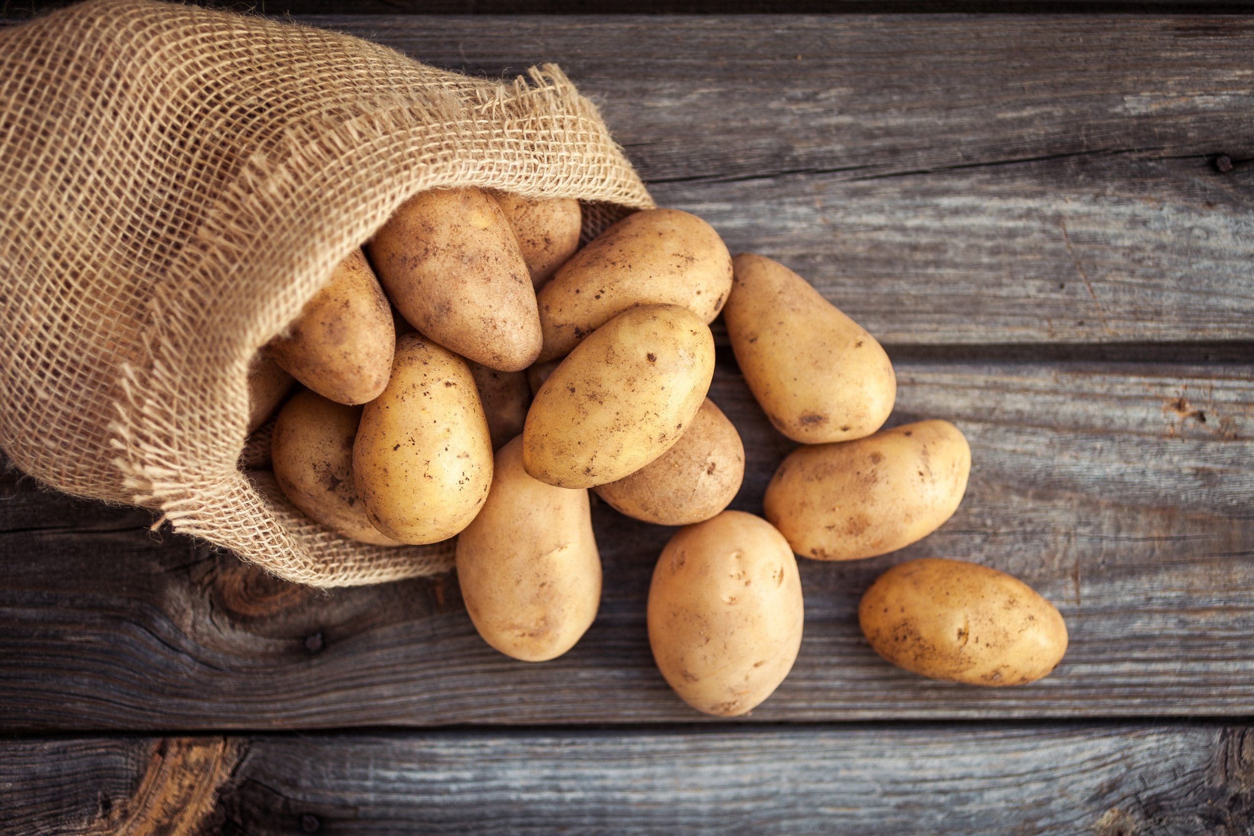 Raw potato food . Fresh potatoes in an old sack on wooden backgr